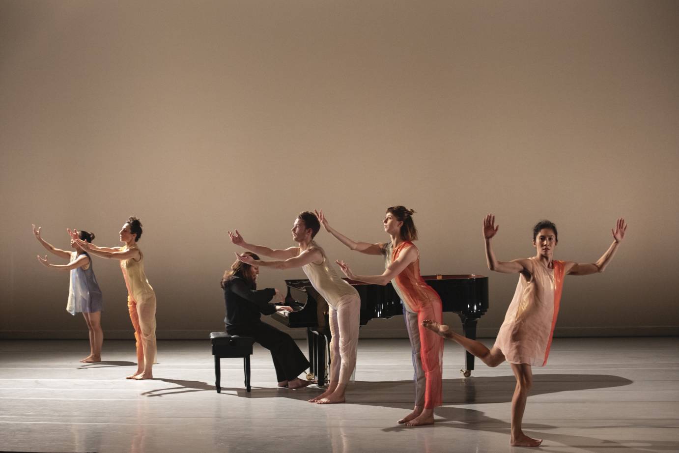 Dancers with curved arms gather around Simone Dinnerstein playing the piano