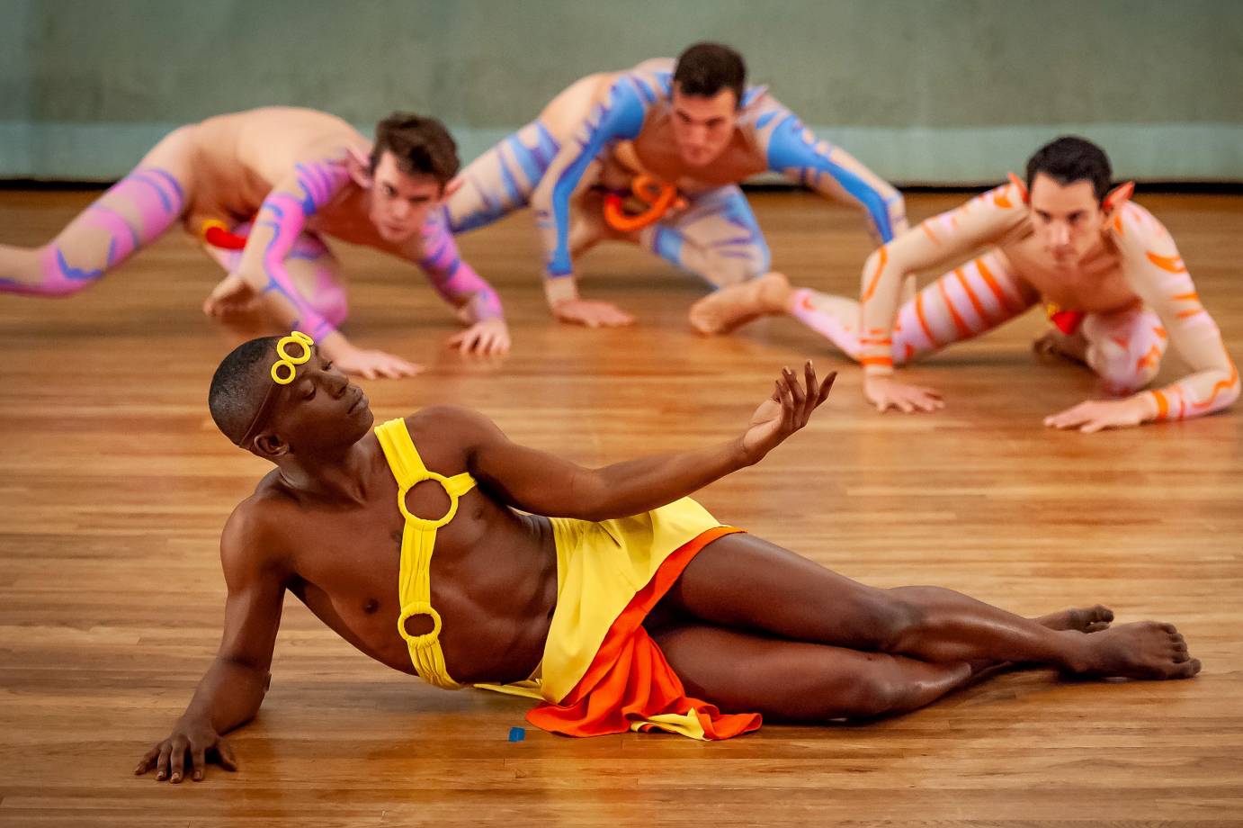 A man in a yellow tunic poses in front of three crawling dancers