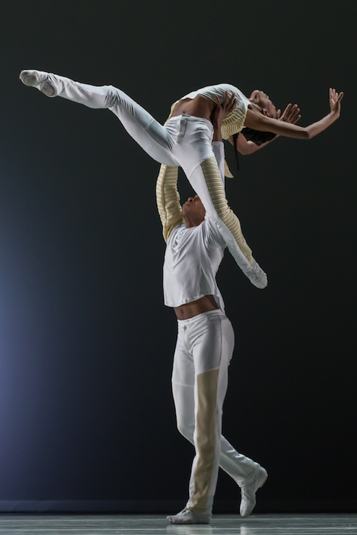 A dancer is lifted by another. Her legs stretch into attitude positions.