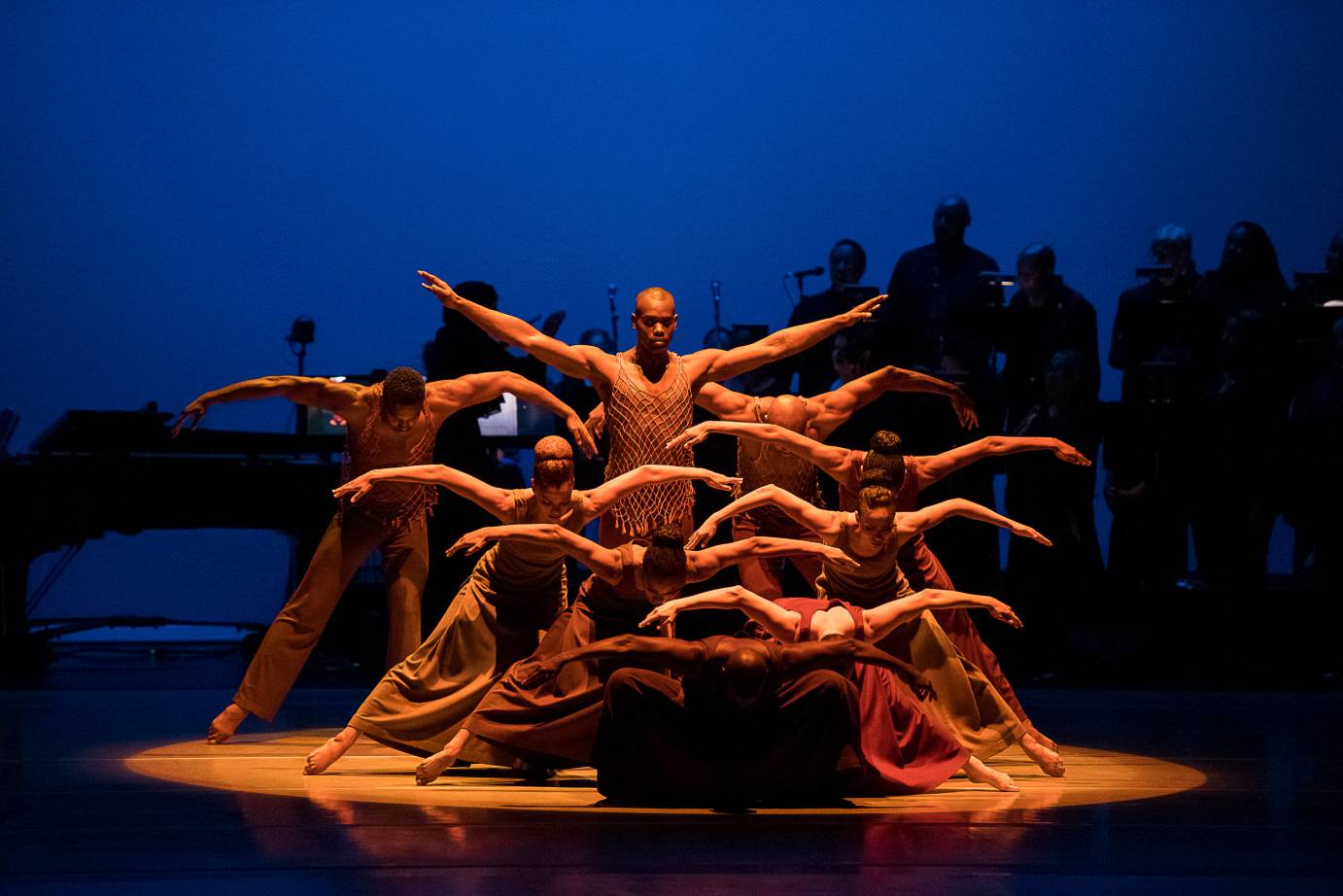 Dancers clump into a pyramid, their arms bent and extended, like wings