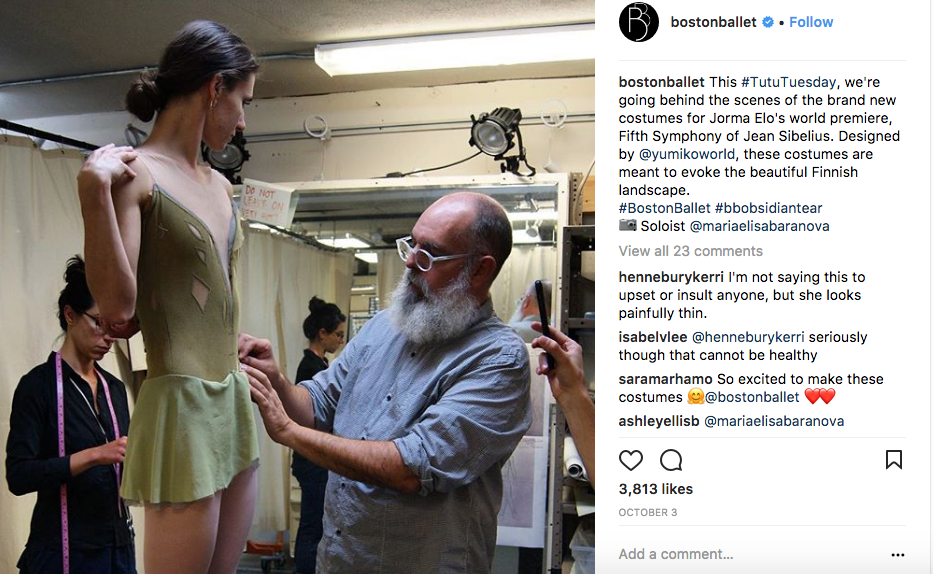 An image from Boston Ballet's instagram page. A costume designer pins a ballet dancer's olive green costume at its skirt.