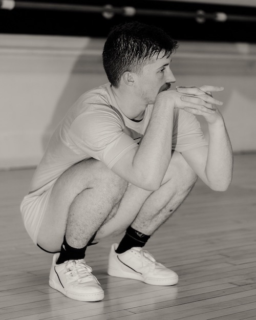 Ashley R.T. Yergens crouches near the floor. His hands are clasped near his face.