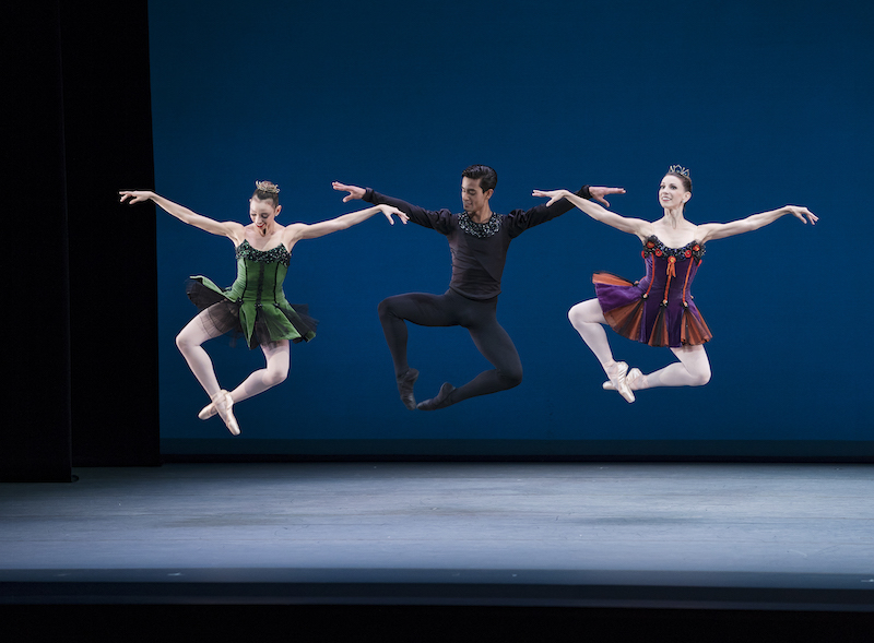 Three dancers leap in the air. Their legs make a diamond shape with their feet crossed at the ankle.
