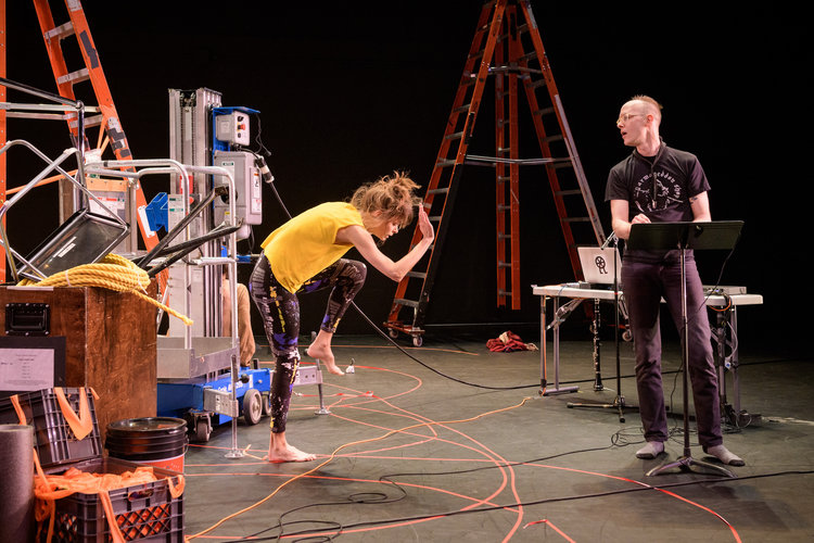 Joanna Kotze bends her body toward the ground while Ryan Seaton stands nearby in front of a music stand