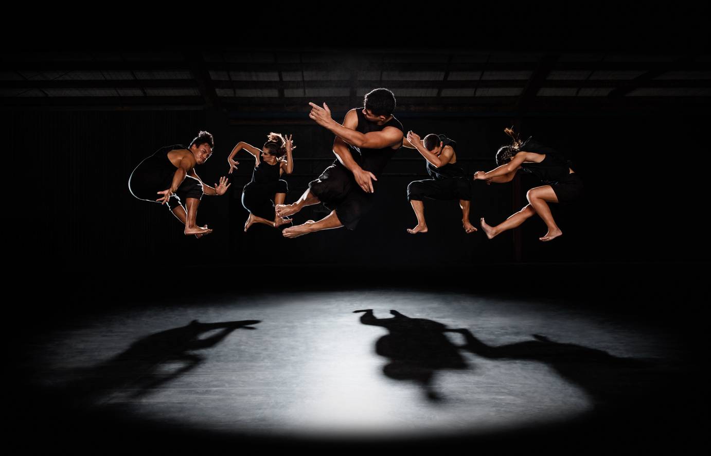 Dancers in black jump into the air, their bodies balled up