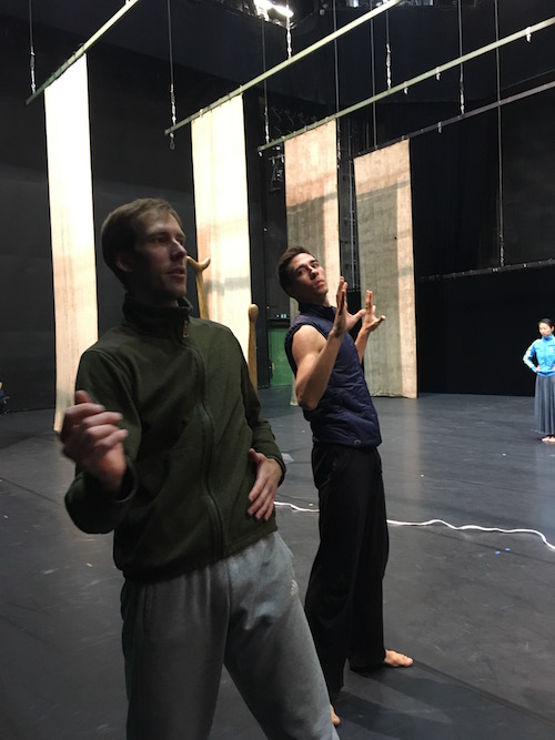 Two male dancers in sweats practice onstage.