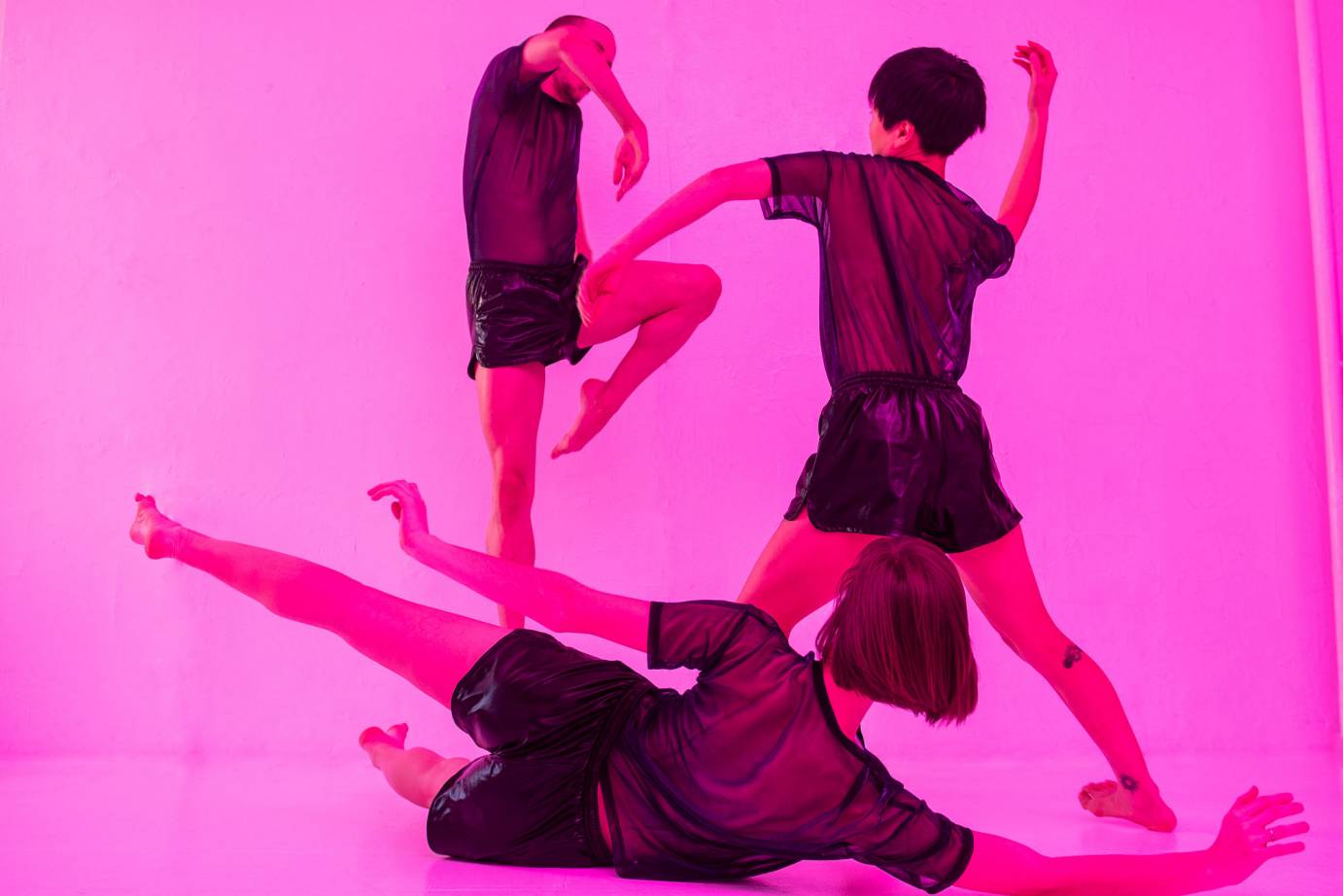 A trio strikes poses against a hot pink background
