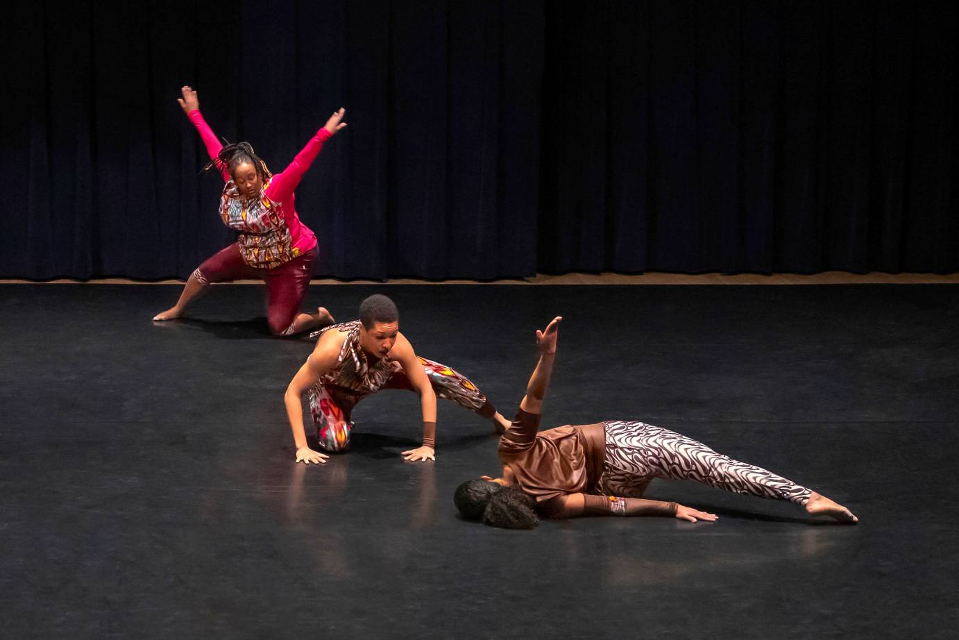 Three dancers range from lying to kneeling in a diagonal line