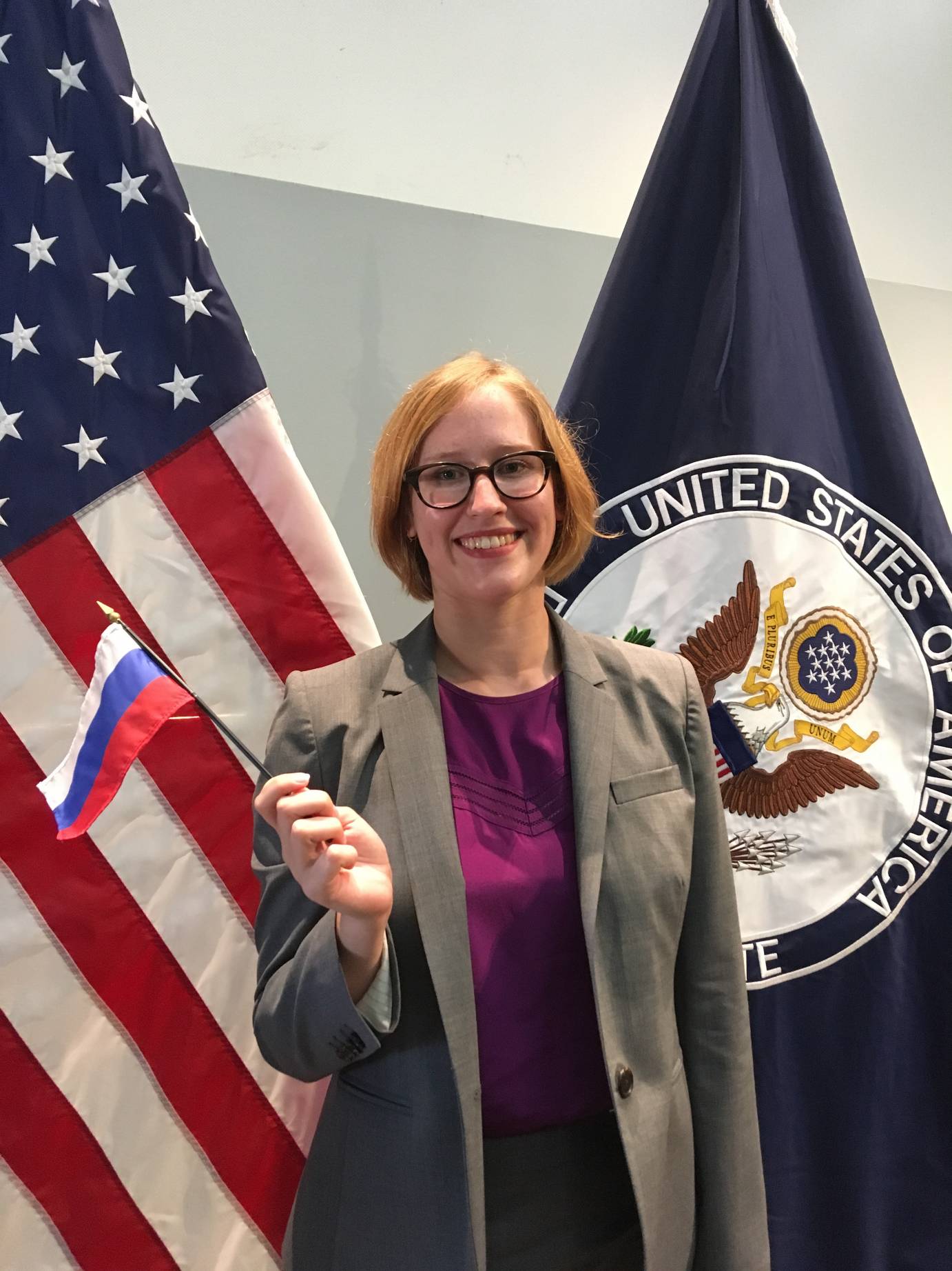 Carissa Landes in business wear at the State Department waving a flag