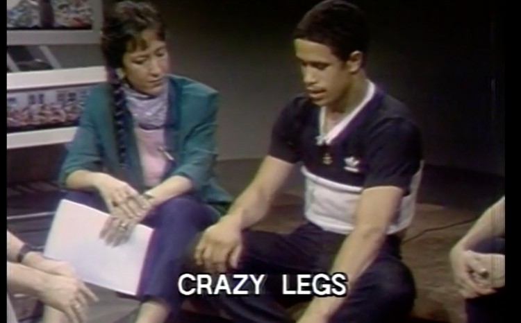 an old tv screen shot of Celia Ipiotis sitting down on the floor with Richard Crazy Legs Colón discussing b-Boying .