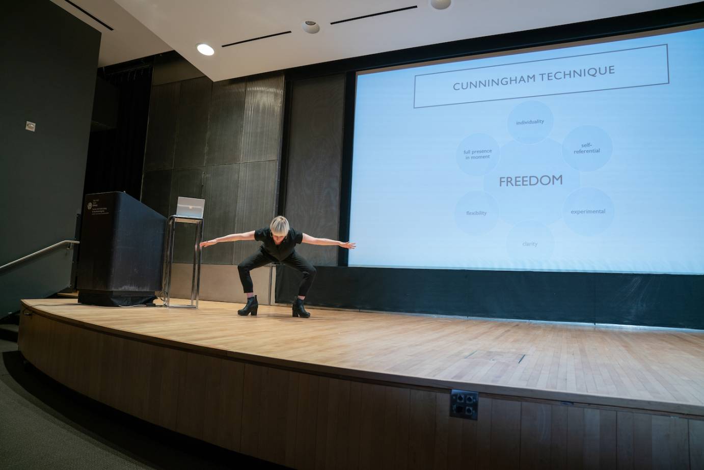 A woman bends in a deep squat against a PowerPoint graphic of Cunningham technique