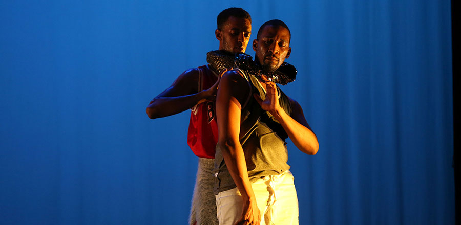 Two dancers on stage, one with his arm wrapped around the other's neck.