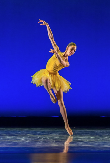 A ballerina in a yellow tutu with one leg raised and the other en pointe.