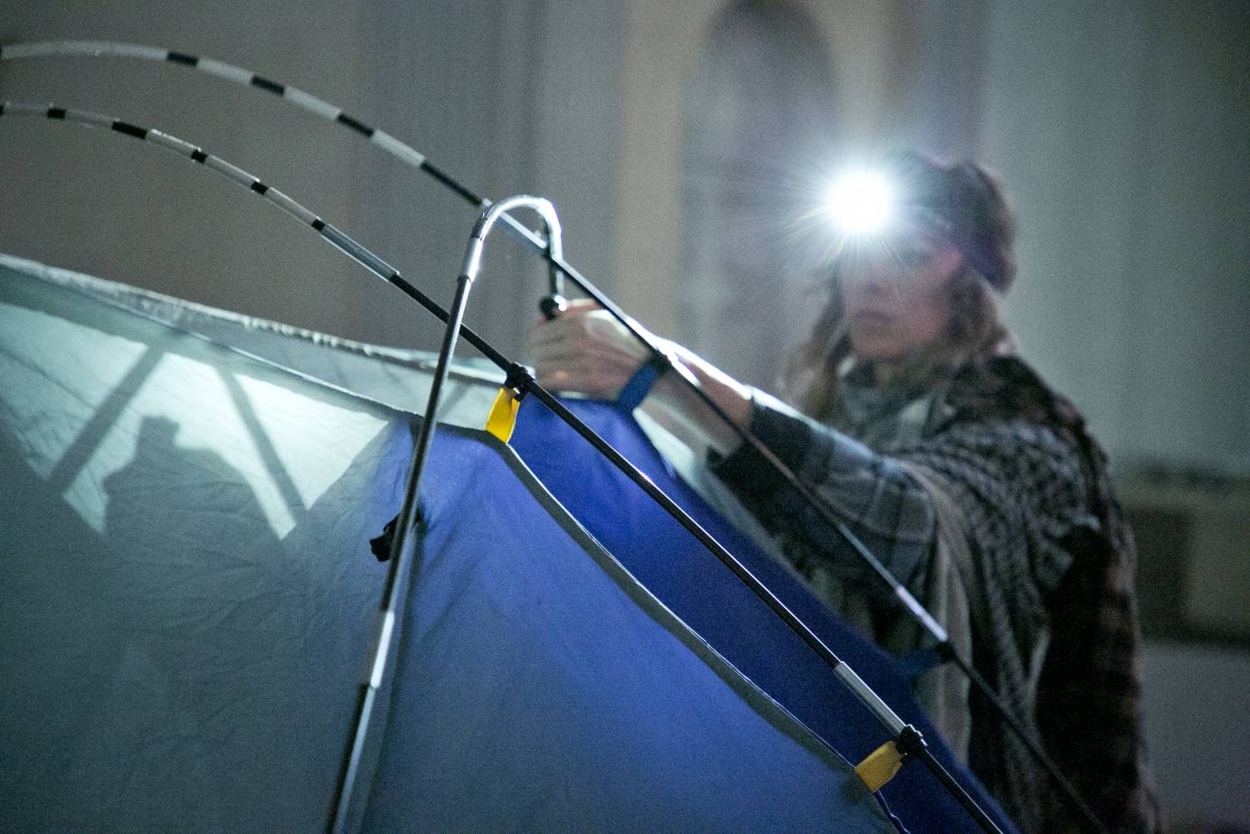 A woman investigates a camping tent while wearing a miner's hat