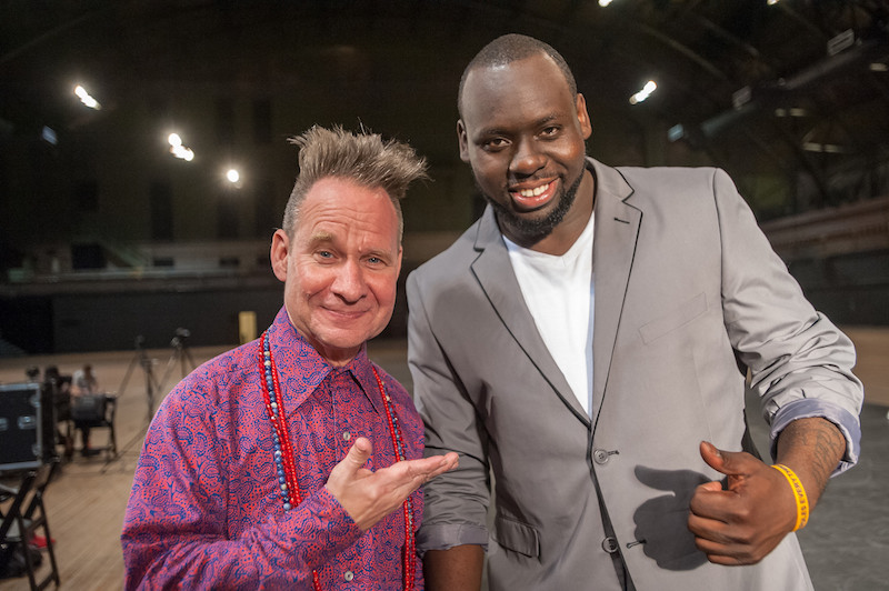 Directors Peter Sellars, in a bright pink and blue button up and beads, and Regg Roc, in a grey suit, pose together