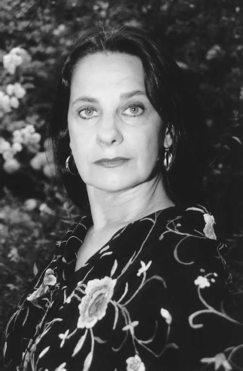 A black and white headshot of Carlota Santana. She sits in front of a floral background and wears a dark floral blouse.