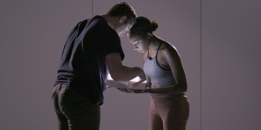 white man, black girl, foreheards pressed together, wearing muted blue and tan colors stare into a rectangular box of light which  they hold in their hands