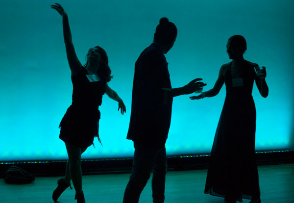 Silhouettes of three dancers against teal lighting.