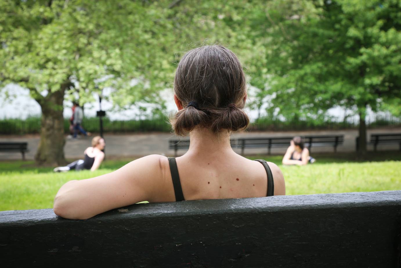 the back of a dancer as she sits on a bench admiring the green trees of Inwood Hill Park