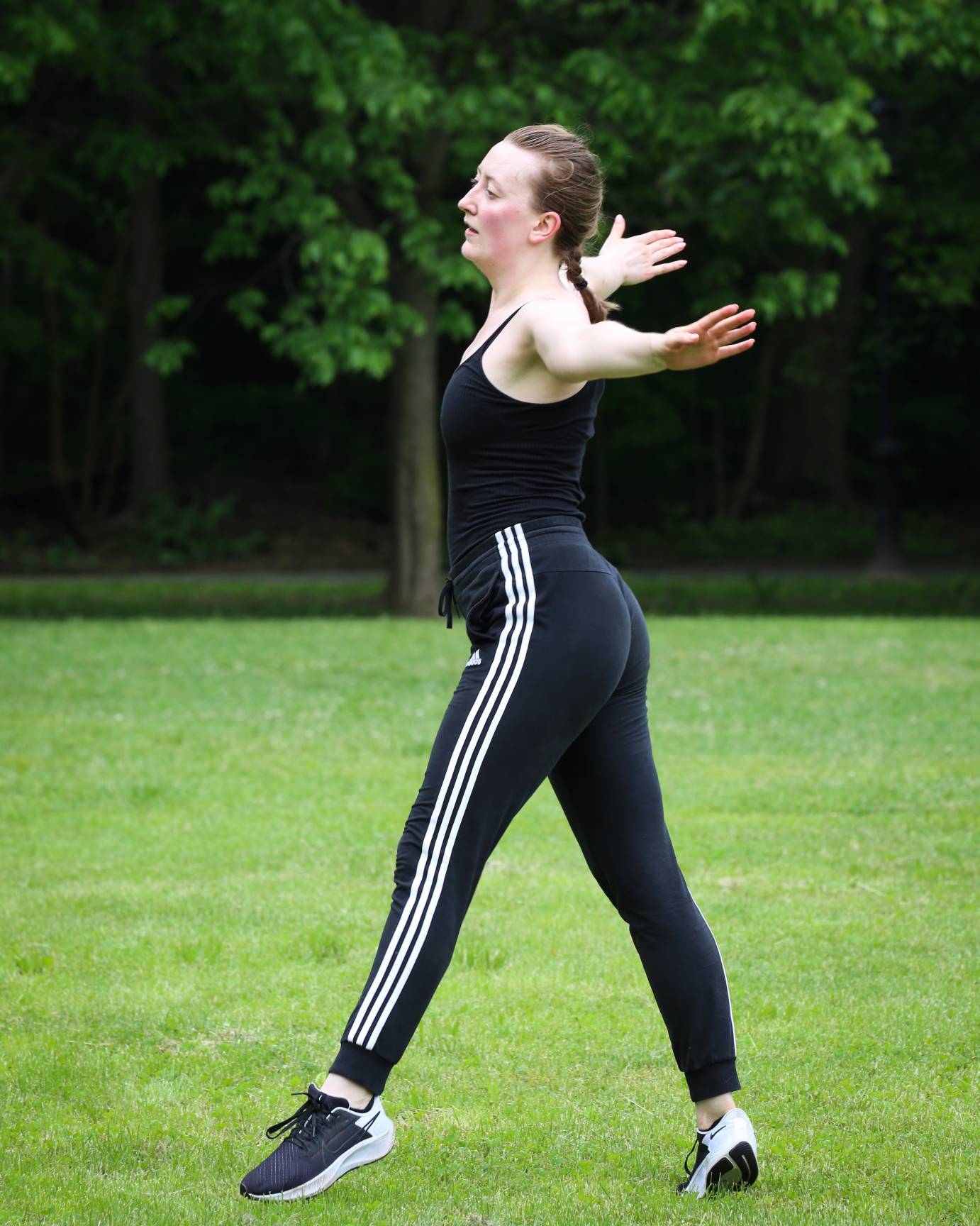 a profie full body view of Garnet Henderson dancing in the park , arms extended out to her sides standing in a wide leg positon in releve