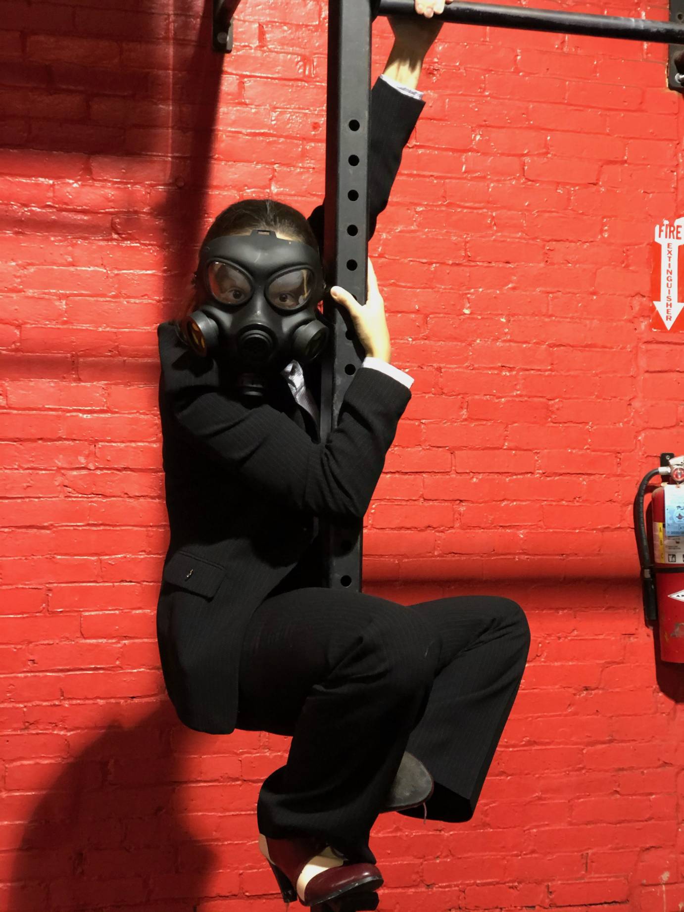 A man in a gas mask hangs on a pole against a red wall