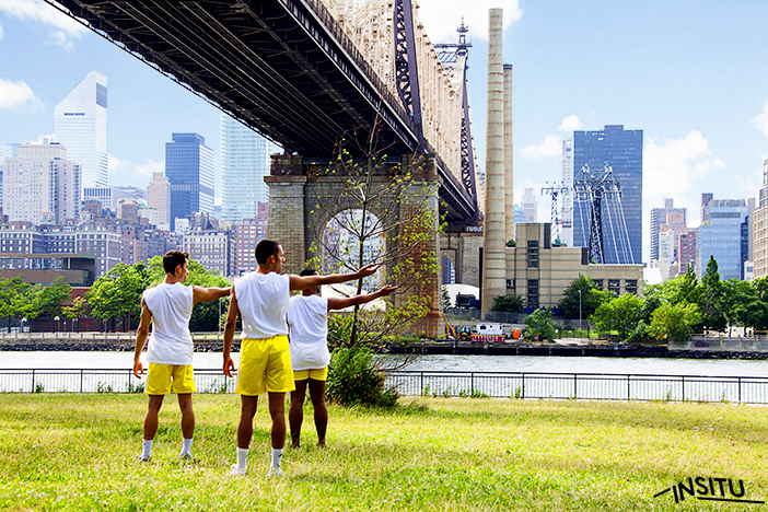 Three male dancers in yellow shorts and white t-shirts stand beneath the Brooklyn Bridge in Brooklyn Bridge Park with their arms outstretched.