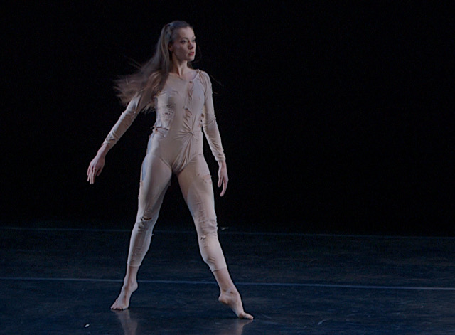 Melissa Toogood stands in a wide relve position wearing a beige unitard onstage in performance for RainForest