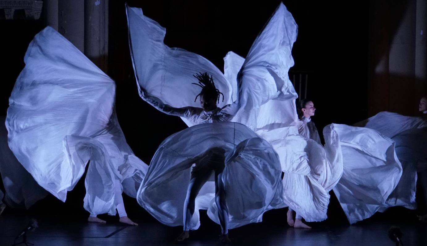 dancers with large expanded costumes in the manner of Loie Fuller swing ands swirl in  their fabric rings creating rushes of wnd