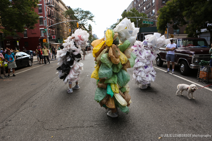 Dancers moving down the street donned in costumes created out of plastic bags. They look like three moving mountains of recyclable bags