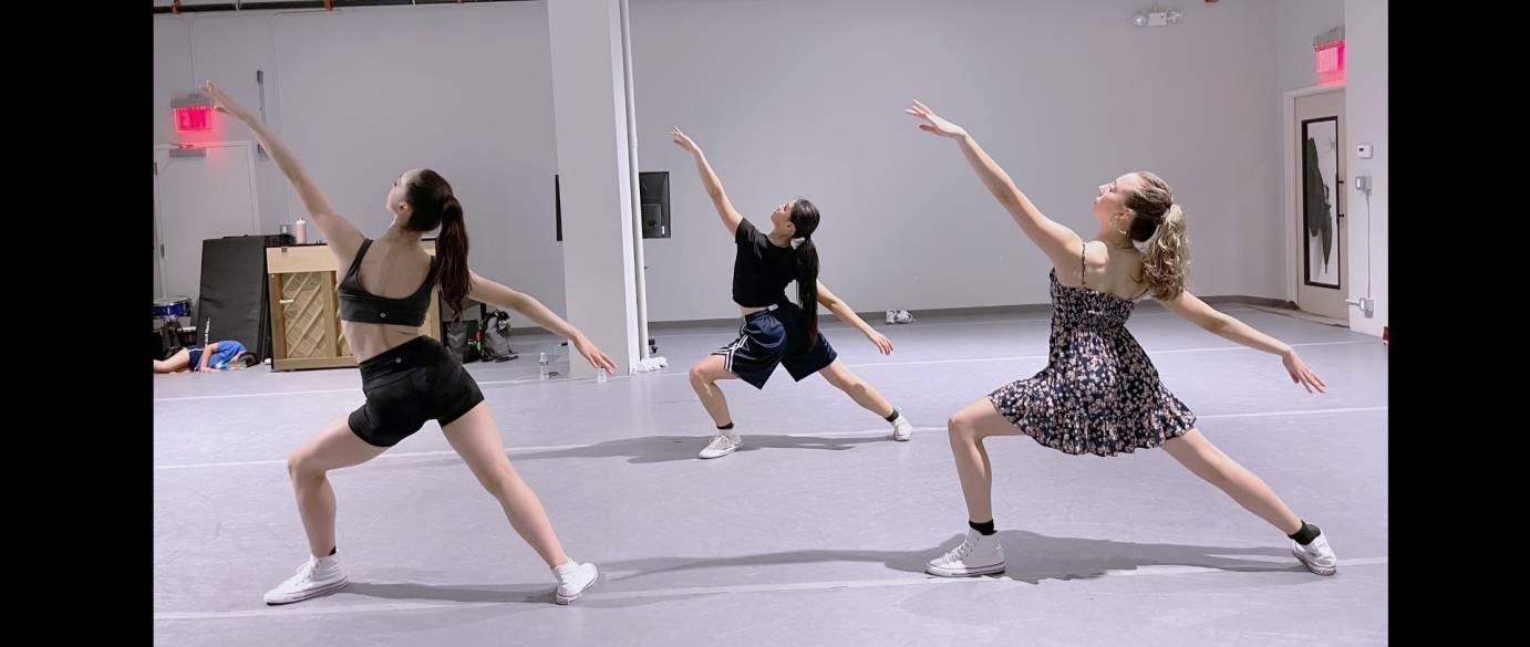 Three female dancers lunge in fourth position, extending one arm forward and the other back on a three-dimensional diagonal