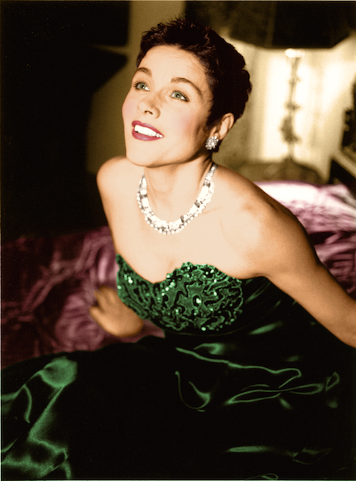 A woman in an emerald strapless dress and sparkly necklace and earrings.