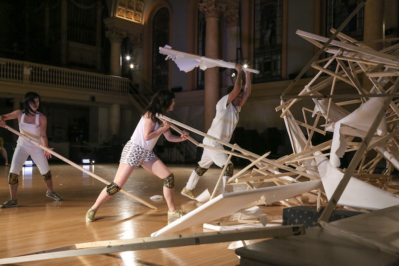 Dancers in white and gold costumes and knee pads destroy the installations
