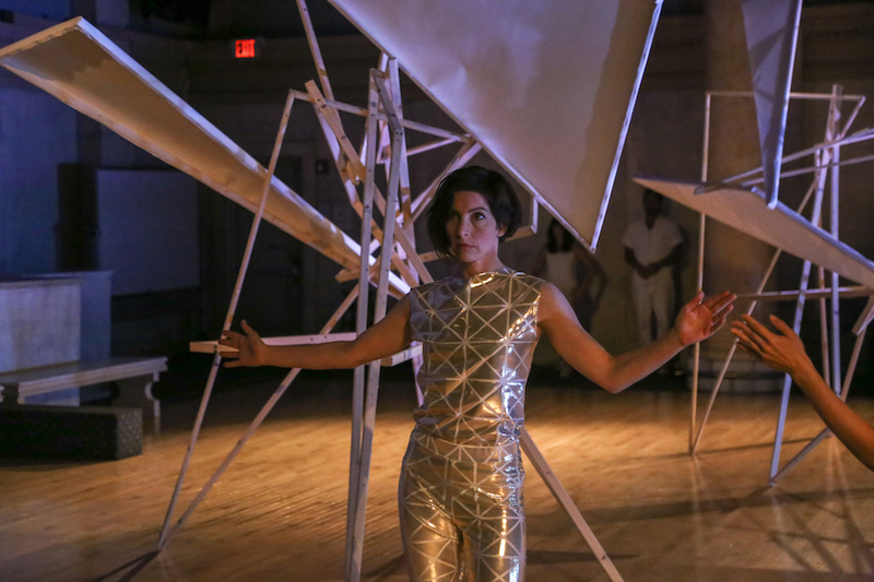 Laura Peterson in a gold lamé fabric top and pants in front of the geometric tepee-like installation