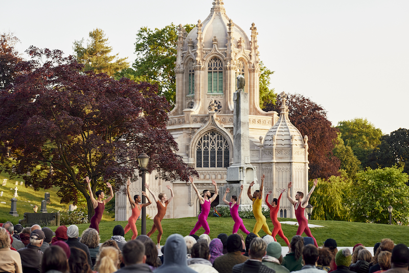 in the majestic peace of Greenwood Cemetery 8 dancers in various bright colored unitards acknowledge each other facing one another in a grouping with arms lifted in exaltation