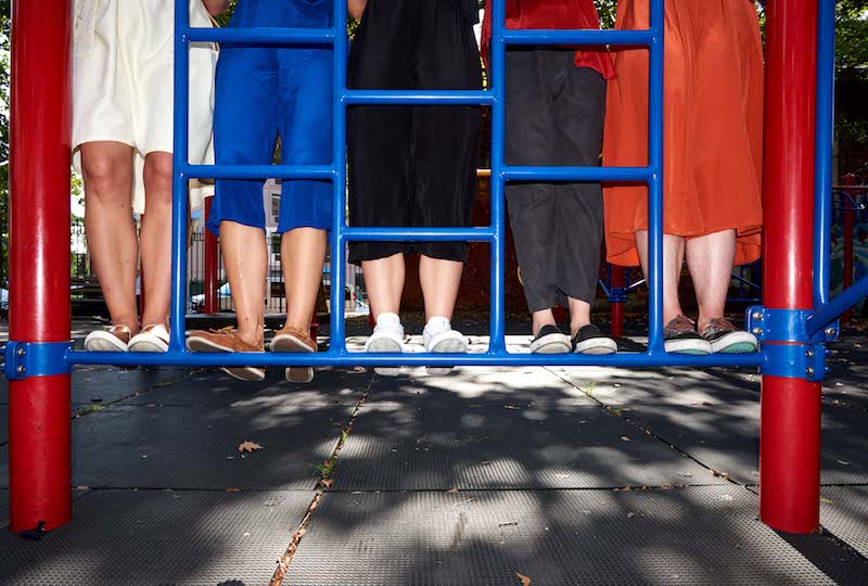 Five individual's feet stand on blue playground bars