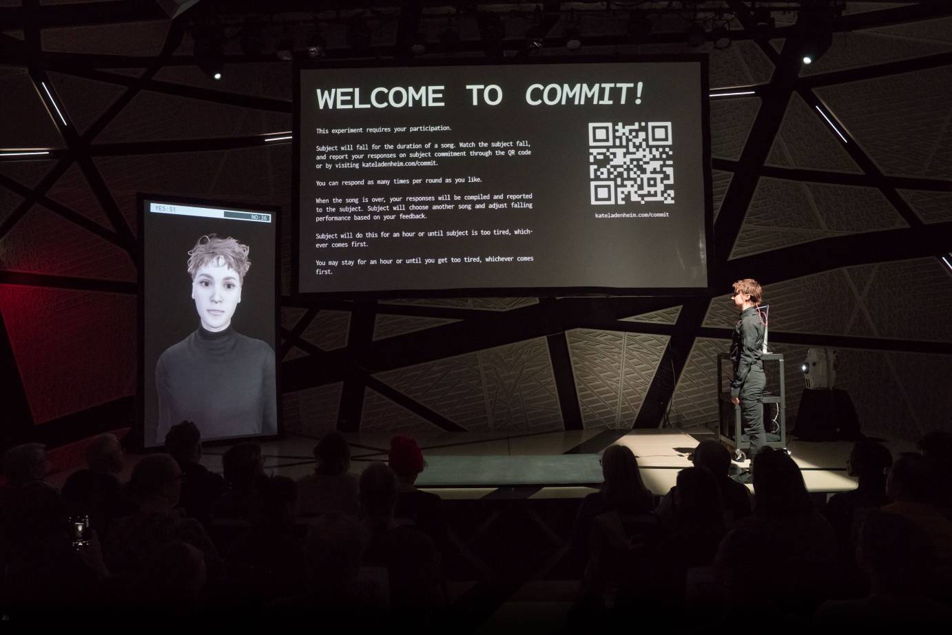 White lettering on a black sign says, WELCOME TO COMMIT! and then lists requirements. The AI photo of a young person with short touseled hair and wearing a black turtleneck looks out at the viewer while that actual person stands to the right of these projections.