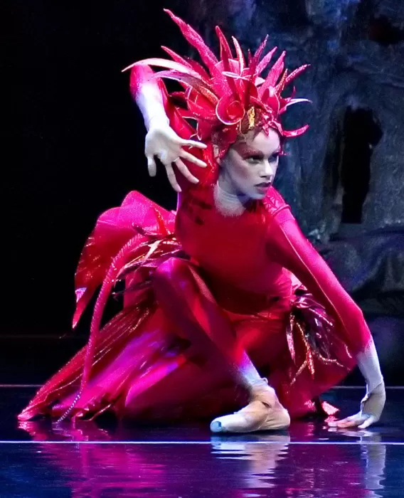 caught in a dramatic pose while perched on the floor, Misty Copeland, donned in a red feather headress and sparking red costume, looks ready to pounce. 