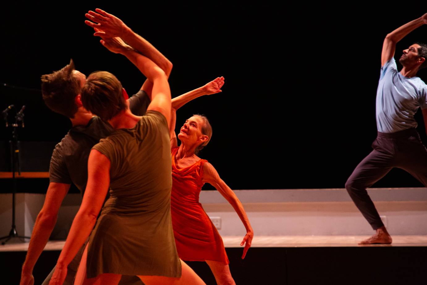 four dancers lunge in profile. one stands on a stage, 3 hit the pose in a cluster facing one another. The trio is on a level below the soloist.