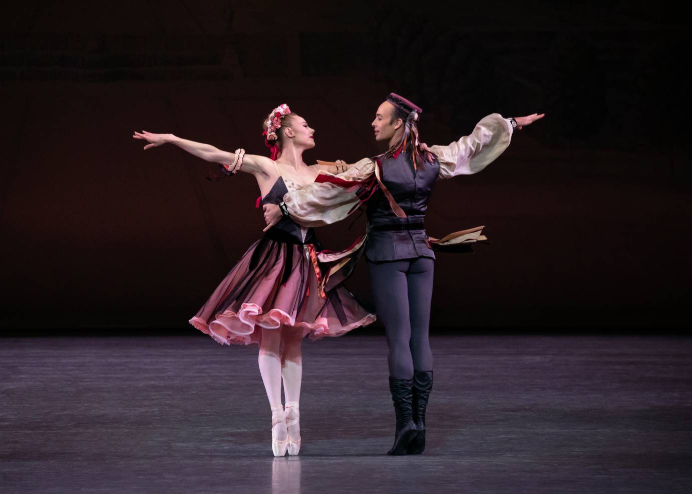 Two dancers in folk costumes hold each other's bodies with one arm; the other is extended