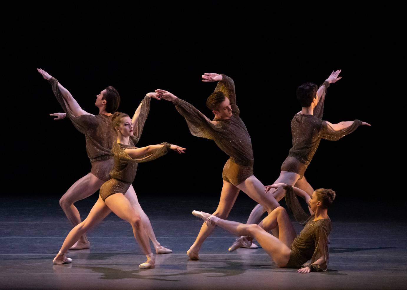 Dancers in brown pose with their arms extended