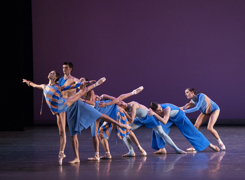 Dancers in blue and orange costumes of various styles are configured in a cascading line