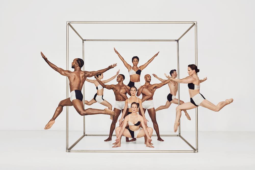 acompany of dancers wearing black and white shorts or blackand white bikinis,pose, and jump in a huge silver frame shaped like a cube