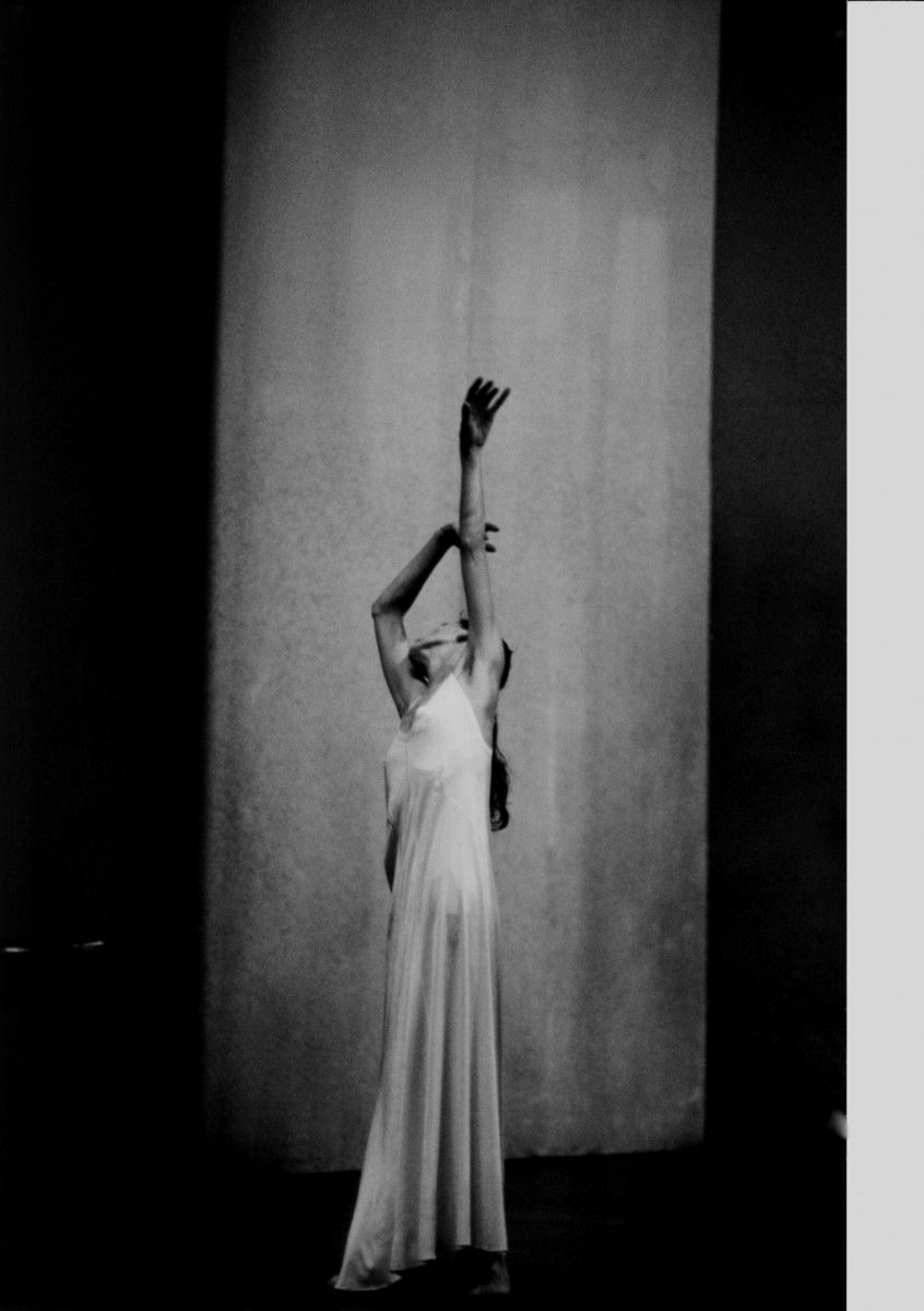 Pina Bausch in a long silk dress lifts her arms above her head.