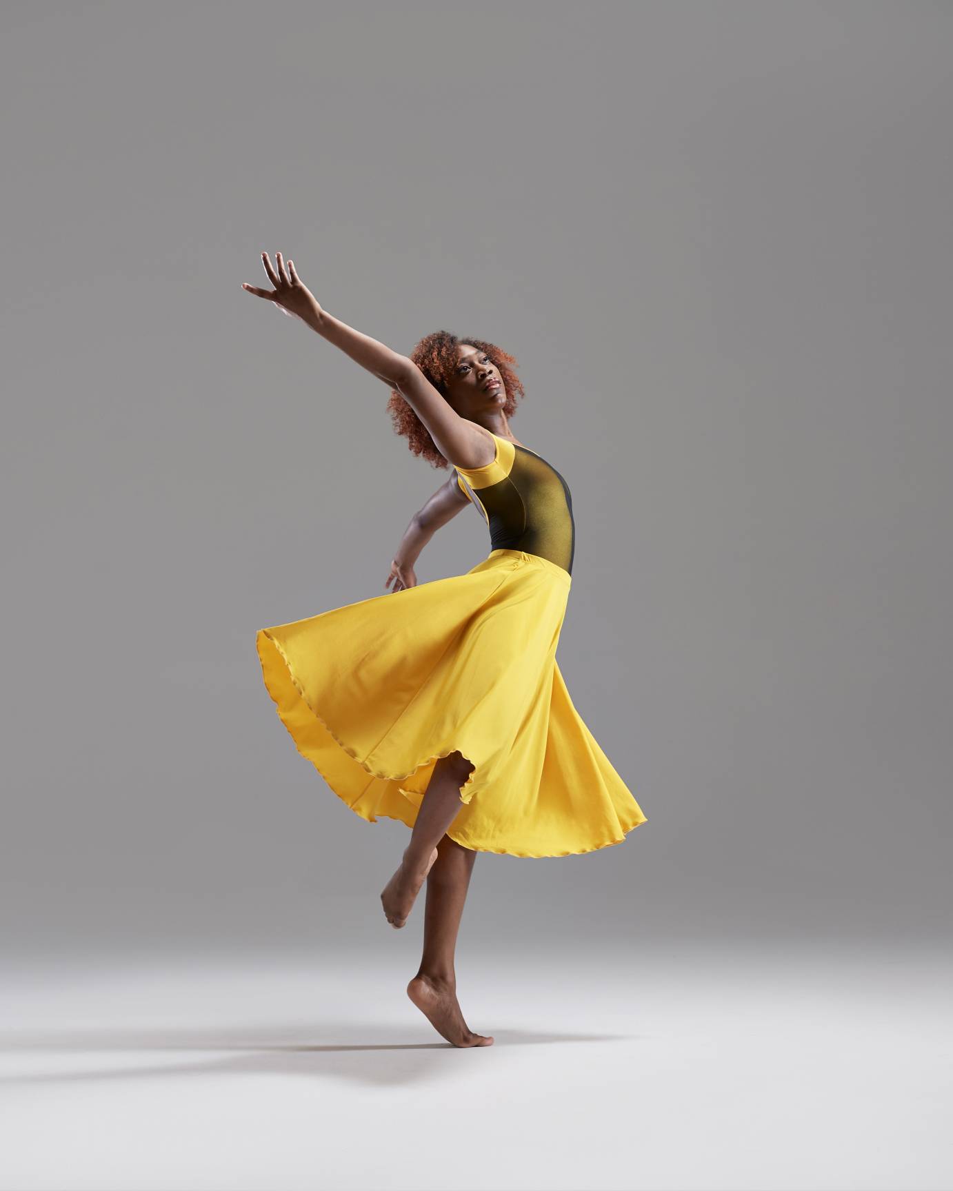 A young woman in a yellow dress swoops in an elegant pose