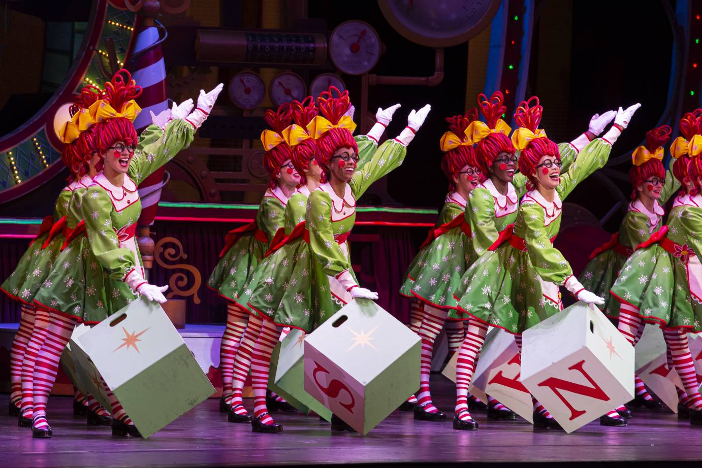 several Rockettes dressed as colorful smilling rag dolls holding wooden boxes with letters on them