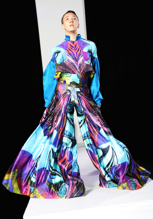 A dancer in a multicolor gown. The gown includes bright purple, shades of blue and neon yellow. The skirt swishes as they walk.