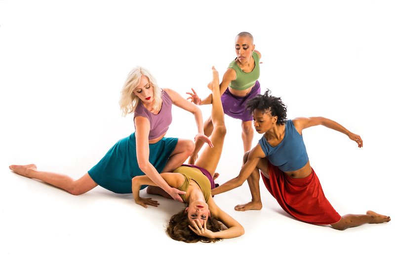 Four women in colorful tanks and skirt spiral and lunge to the ground. One woman lays on her back.