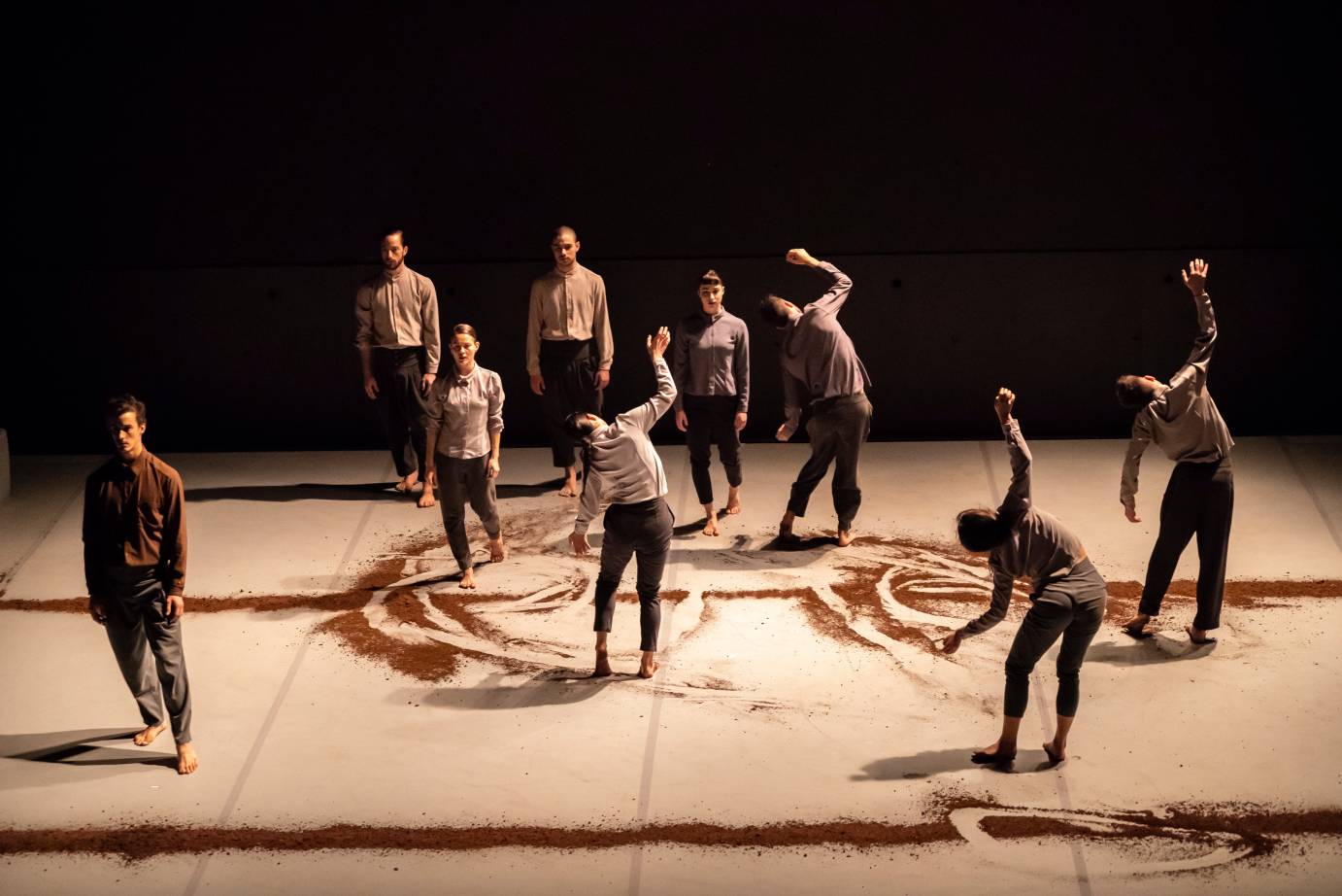 Nine dancers stand among furrows of dirt