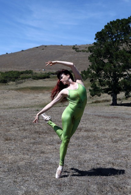 A red-haired woman dances on a grassy field en pointe