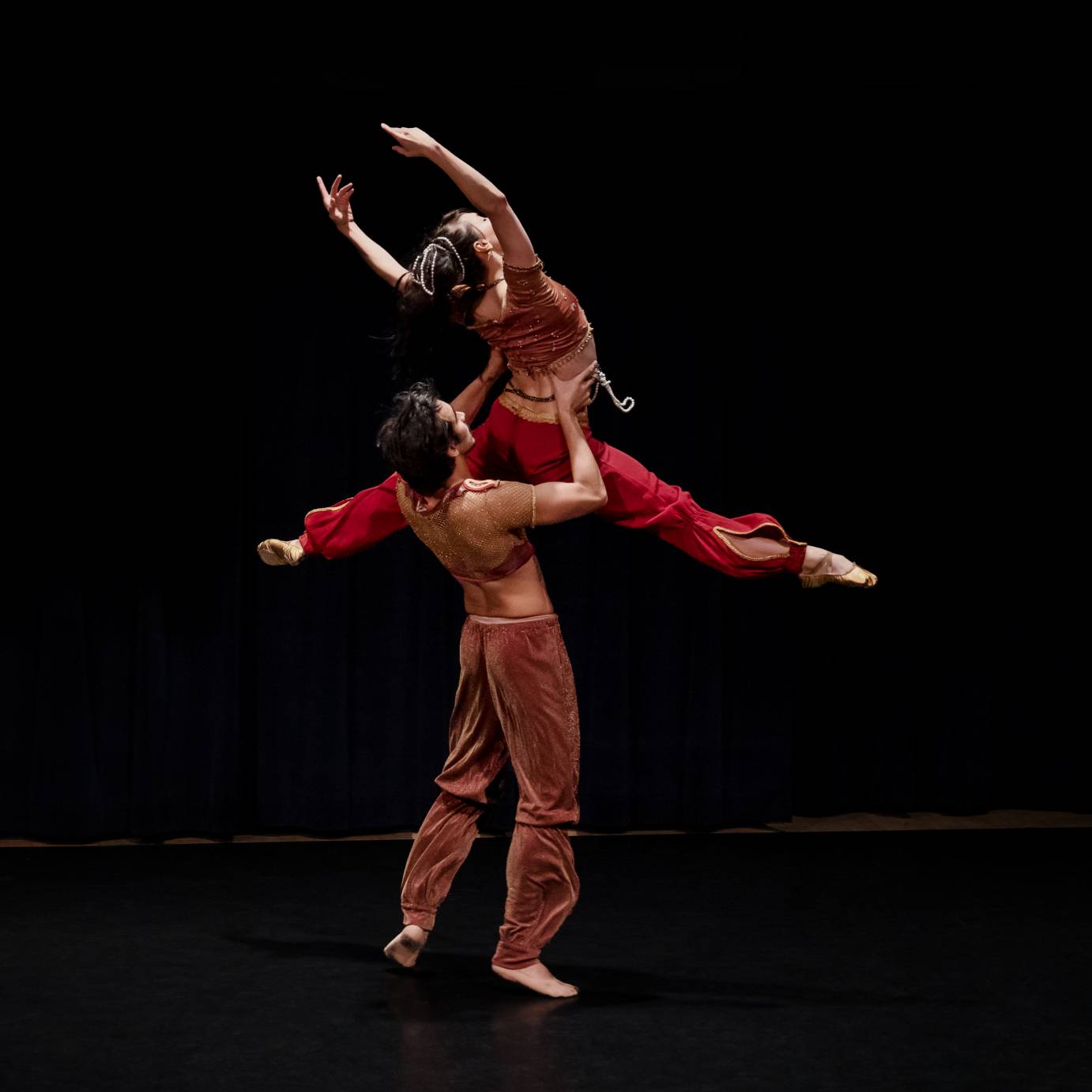 A man lifts a woman into the air, her legs split, her arms lifted